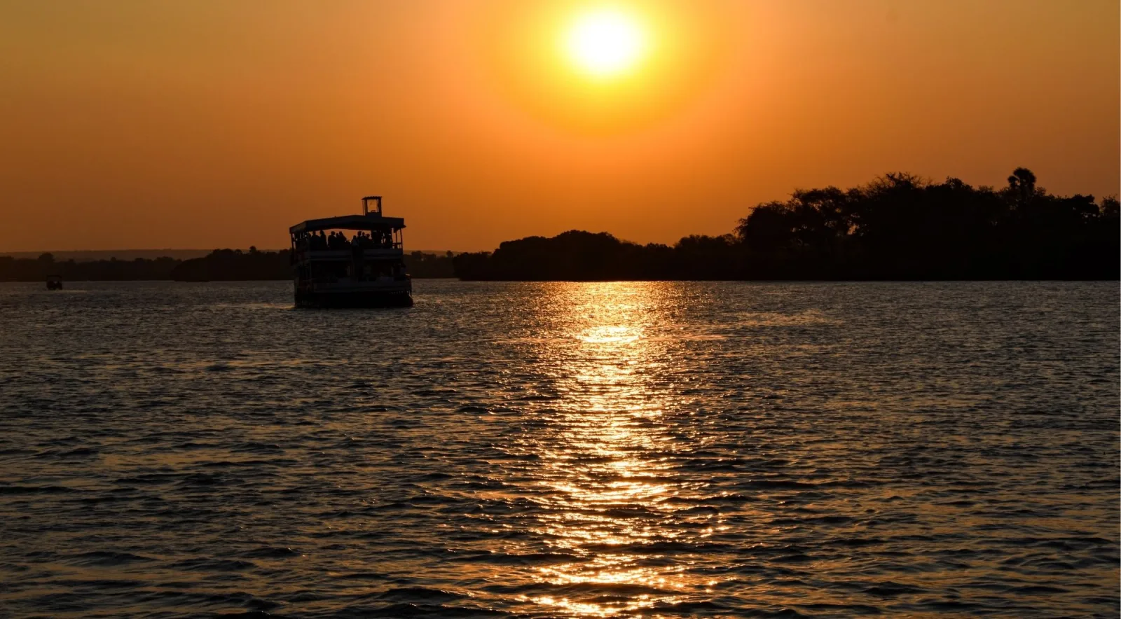 Cruise boat silhouetted against a brilliant orange and red sunset on the Zambezi River at Victoria Falls